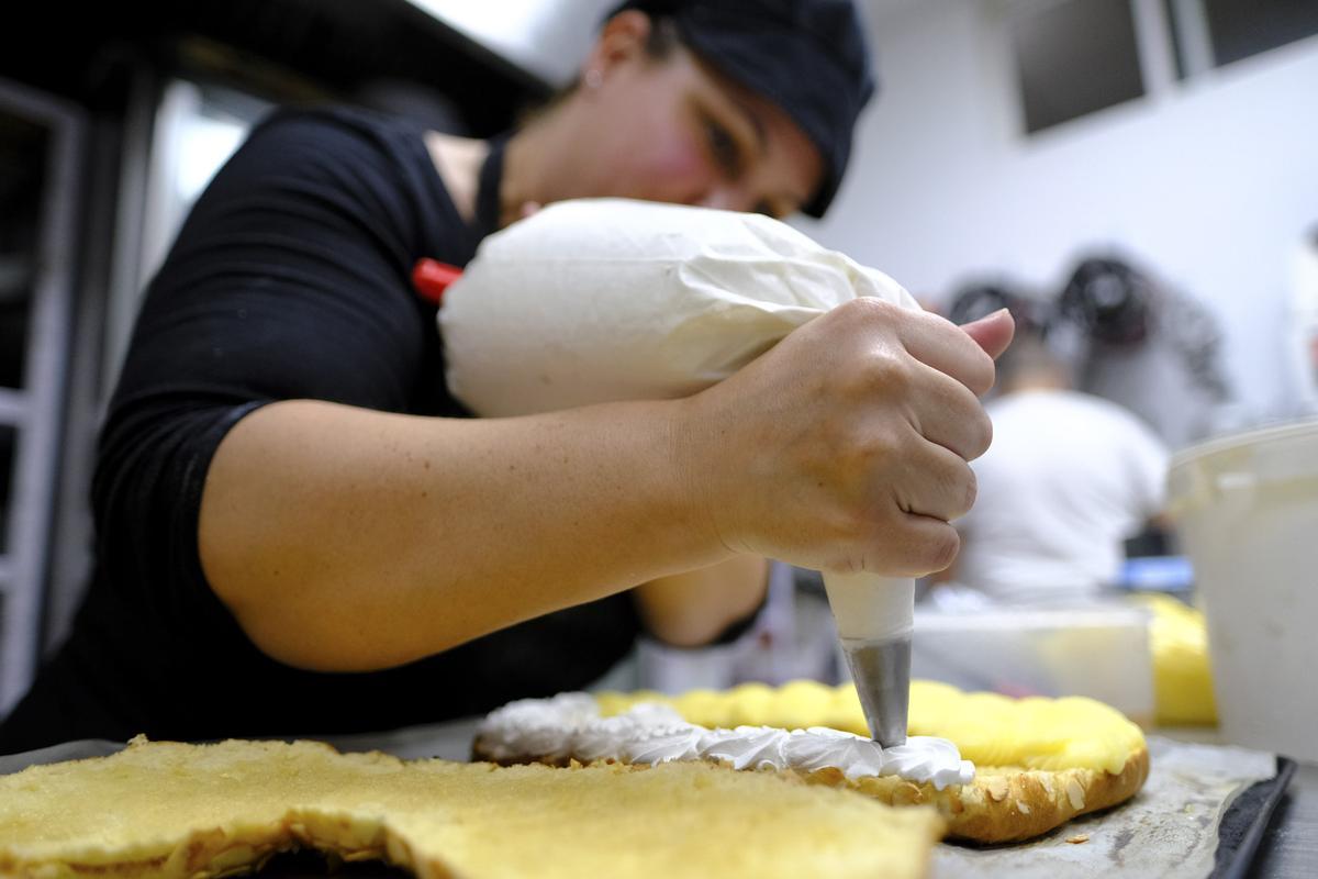 Ana, pastelera de Hijo de Rosarito, rellena con crema y nata un roscón de Reyes para un encargo