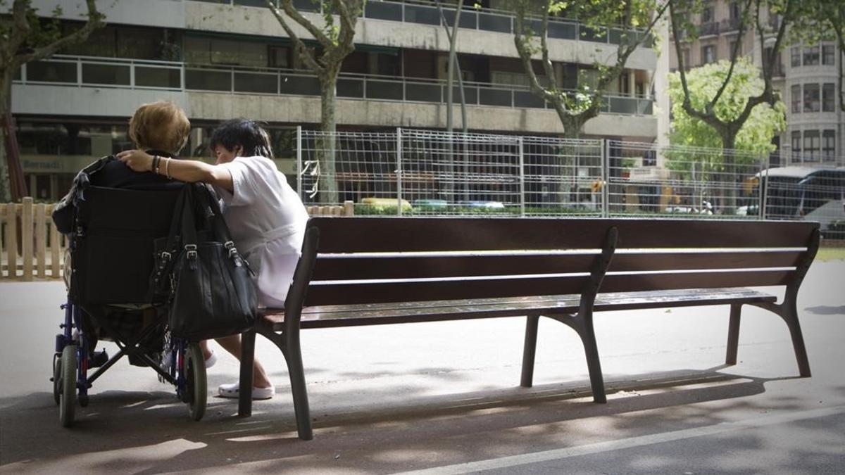 Un anciano con su cuidador en el paseo de Sant Joan en Barcelona.