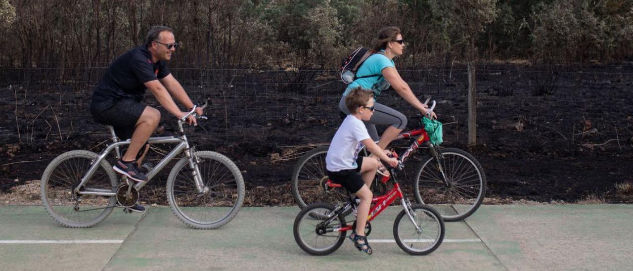 Una familia pasea en bicicleta por la zona afectada por el incendio. |