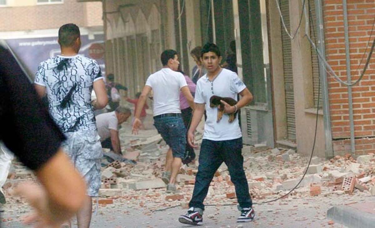 Un noi protegeix un cadell mentre la gent corre pel carrer uns instants després del terratrèmol que ha afectat la tercera ciutat en població de la regió de Múrcia.