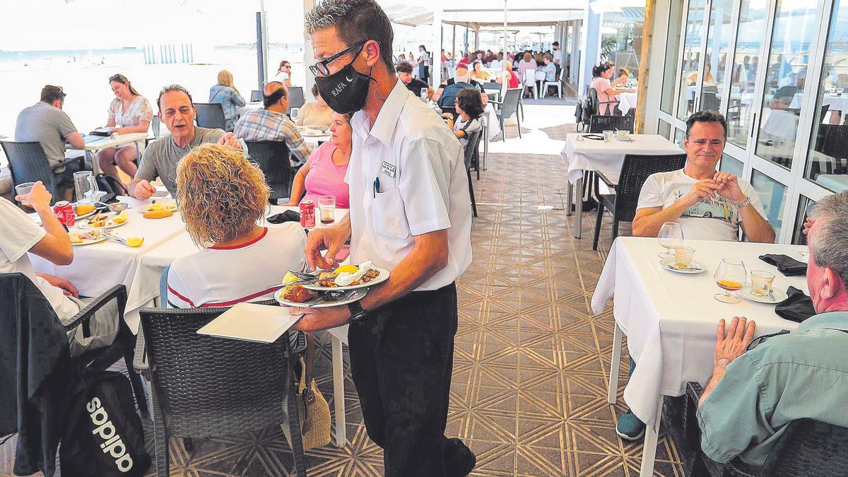 Un camarero sirve unas mesas en la terraza de un restaurante.