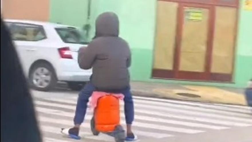 En patinete, en chanclas y sentado sobre una bombona de butano