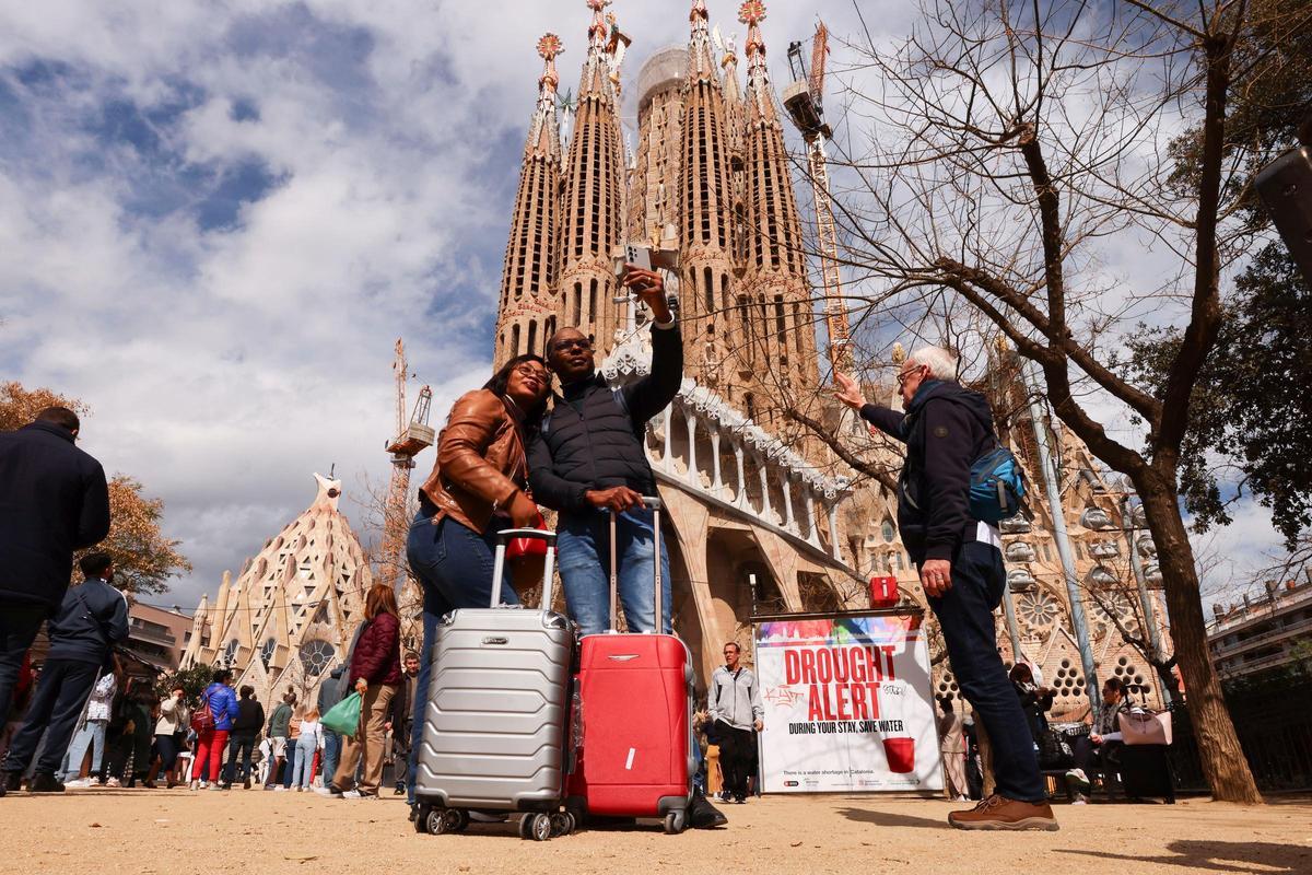 Turistas se toman un selfie junto a un cartel en la Basílica de la Sagrada Familia de Barcelona
