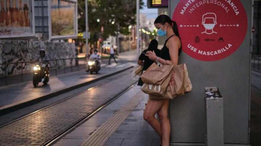 Una mujer espera el tranvía en Tenerife que ha añadido recomendaciones sanitarias en sus paradas.