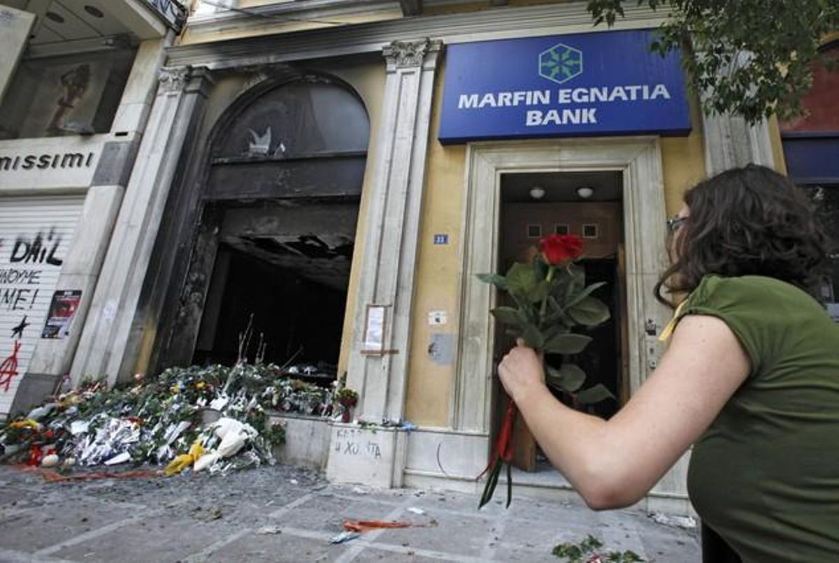 A woman arrives to place a flower outside a bank that was set on fire during demonstrations over austerity measures in Athens