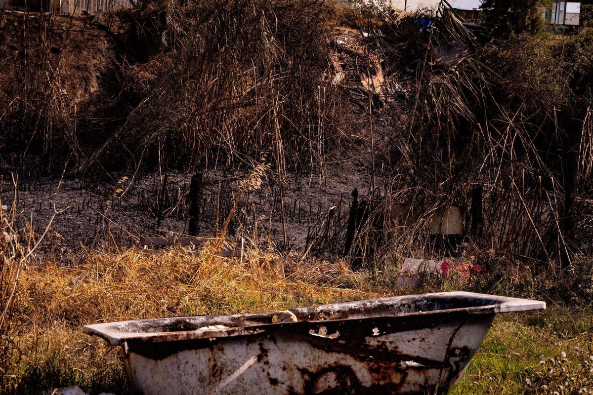 El 1 de julio de 2025, un día después del incendio en la zona de barracas cercana al Port de Barcelona, se observan áreas donde antes había viviendas ahora cubiertas por tierra negra de cenizas. Entre los escombros, una bañera aparece visible, afectada por el fuego que arrasó la zona el día anterior.