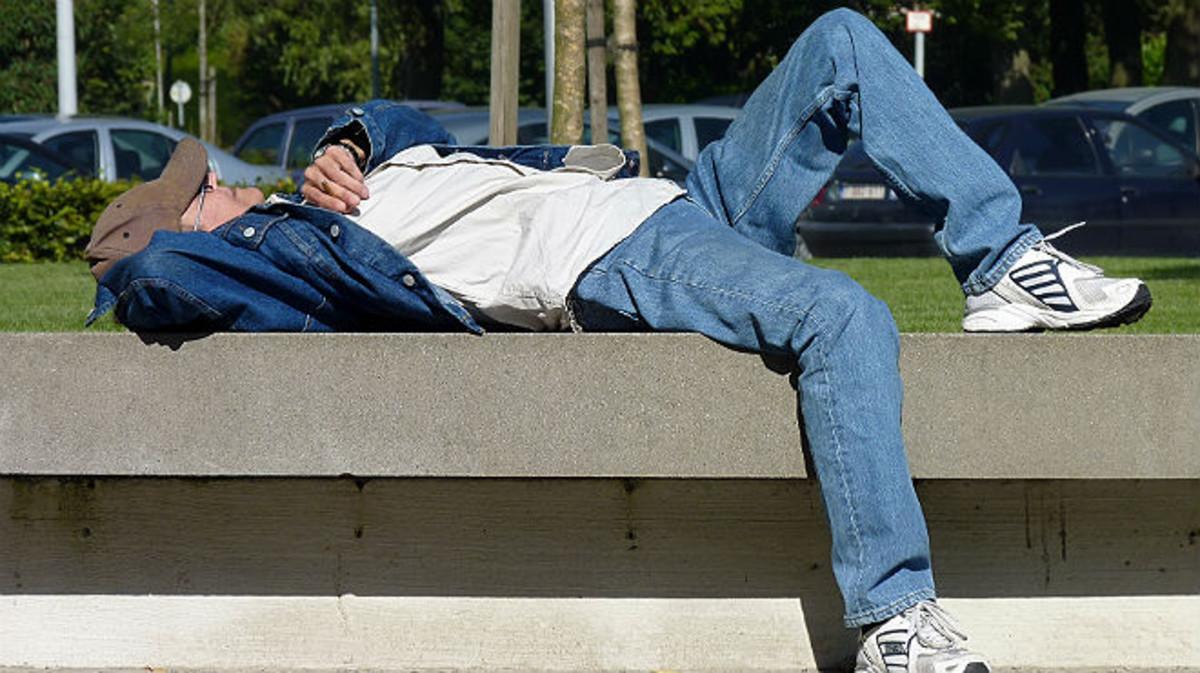Un hombre echa una cabezadita en un parque. Un hombre echa una cabezadita en un parque.