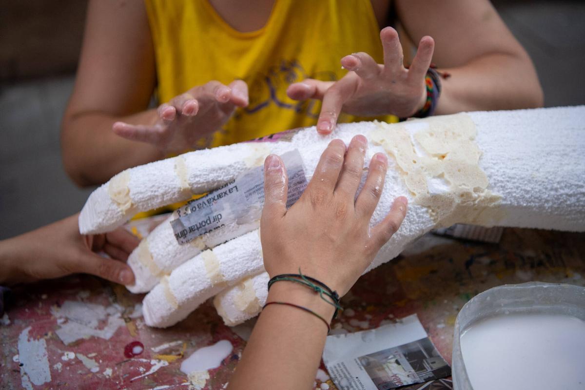 Dos vecinas de la calle Tordera creando la textura de una mano gigante con papel de periódico y cola para un decorado de ‘El Señor de los Anillos’ de las fiestas de Gràcia