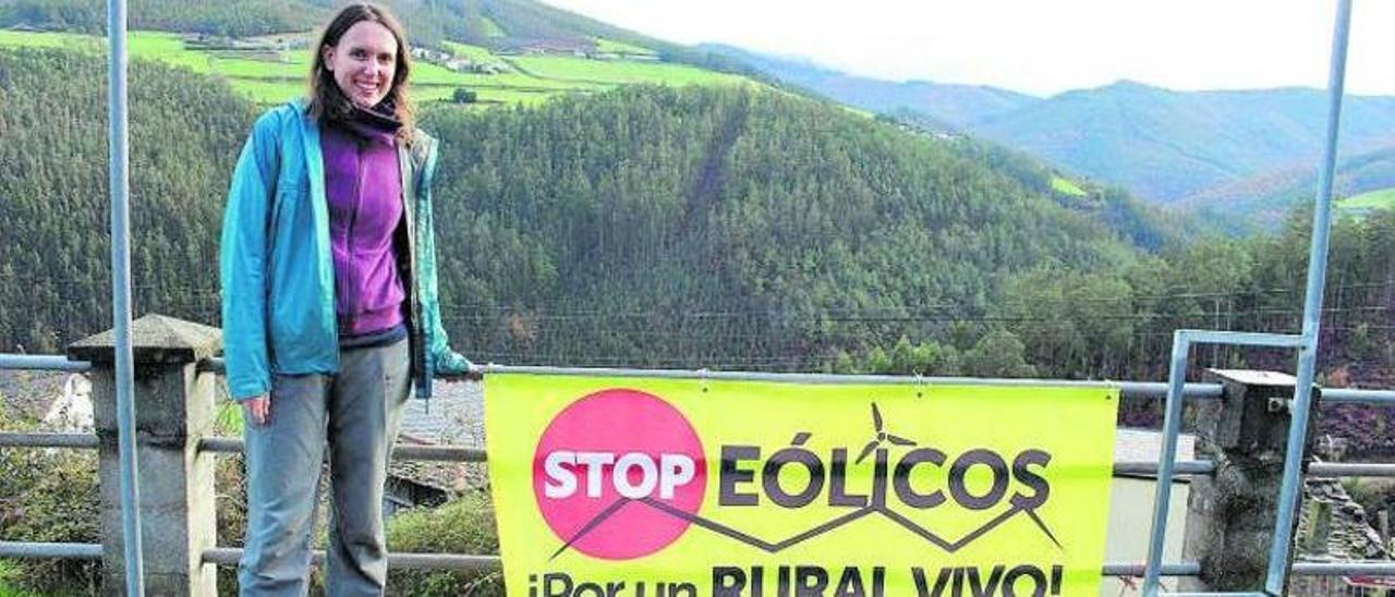 Carmen Molejón, en la localidad santirseña de Lourido, con una pancarta y con los cordales donde se planifican varios parques eólicos al fondo. | T. Cascudo