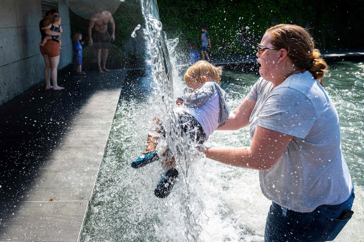 Una mujer refresca a su hijo en una fuente en un parque en Washington DC.