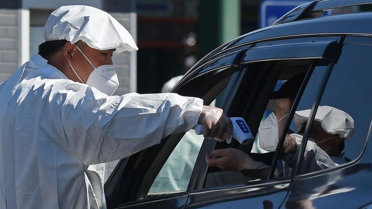 El trabajador de un cementerio de Pekín toma la temperatura a un conductor antes de que acceda al recinto.