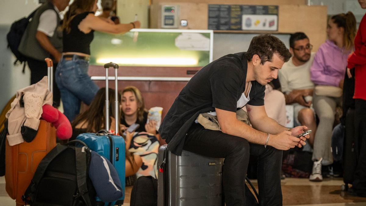 Un hombre, sentado sobre su maleta, consulta el teléfono móvil mientras espera en el aeropuerto Tenerife Norte-Ciudad de La Laguna.