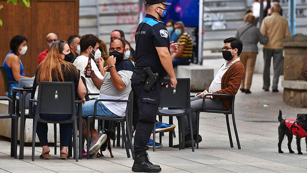 Un policía local, vigilando el cumplimiento de las restricciones en una terraza. |   // CARLOS PARDELLAS