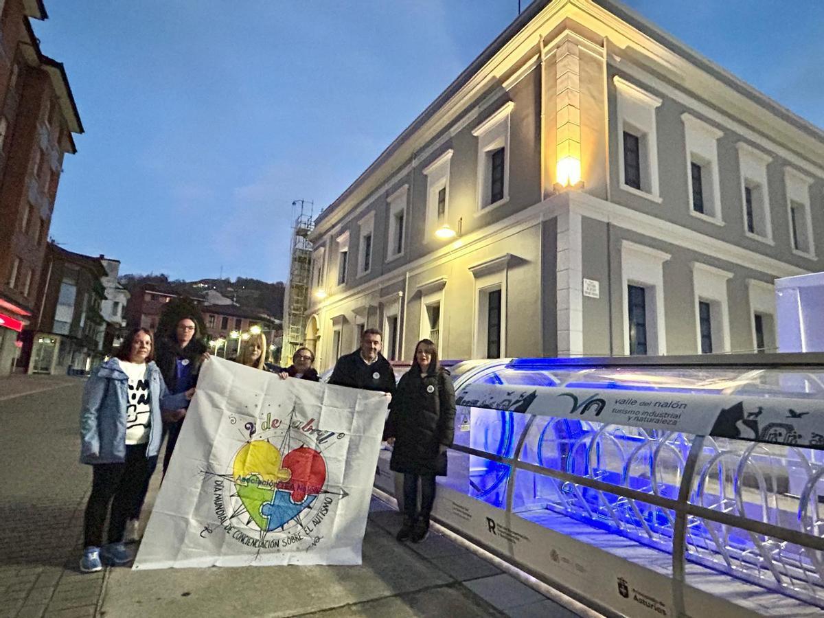 El alcalde de Laviana, Julio García, a la derecha, junto a miembros de la asociación TEA Nalón con el aparcabicis iluminado de azul