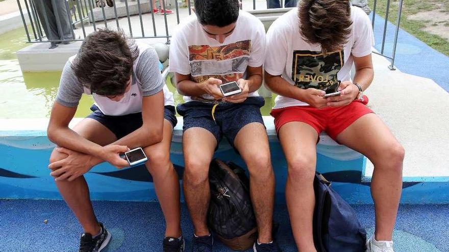 Varios adolescentes &#039;navegan&#039; por internet con su móvil.