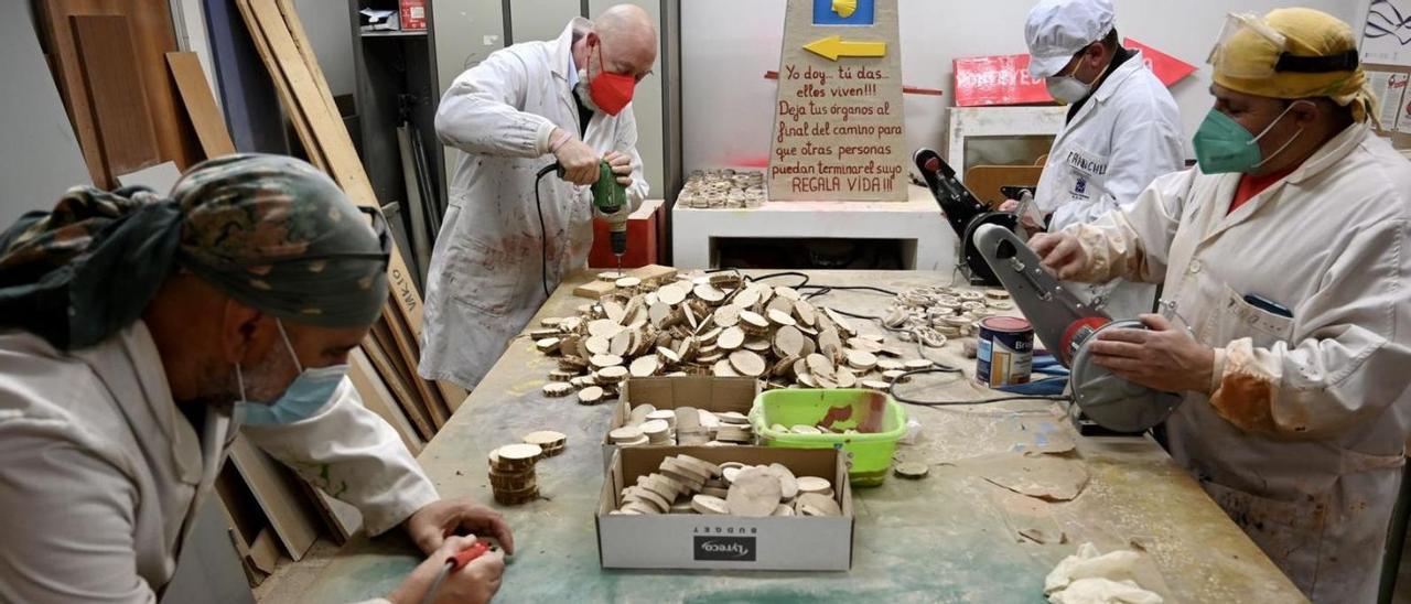 Cuatro voluntarios trabajan creando los dorsales de madera en la Casa Azul. // RAFA VÁZQUEZ