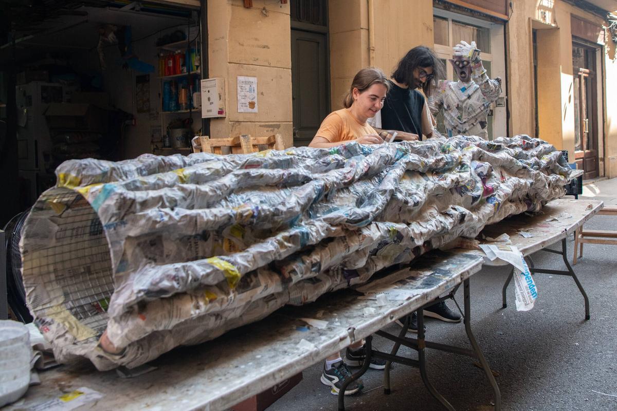 Dos vecinos de la calle Llibertat, creando un tronco de árbol gigante para los ‘guarnits’ de las fiestas mayores de Gràcia. Este año, 5 calles del barrio se han unido bajo la temática de ‘El Señor de los Anillos’. Barcelona, 4 de agosto de 2026. Foto: Belén González / EP