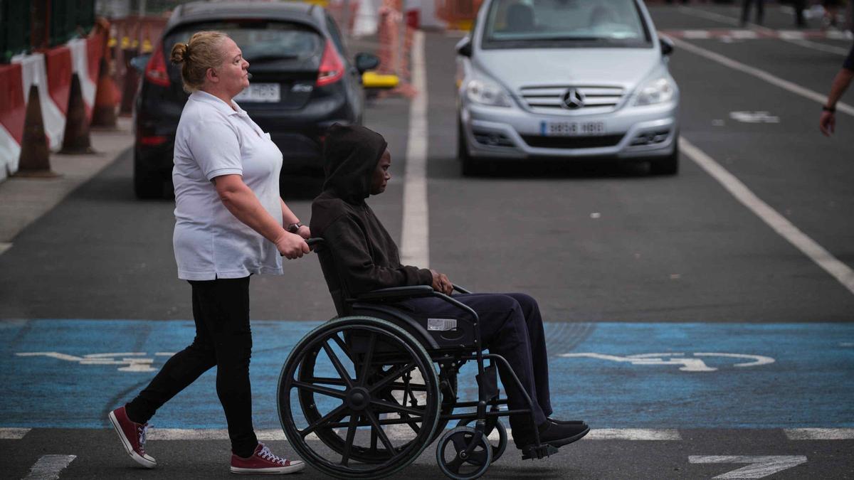 Personal de servicios sociales lleva en silla de ruedas a un migrante que llegó en malas condiciones a Tenerife en un cayuco.