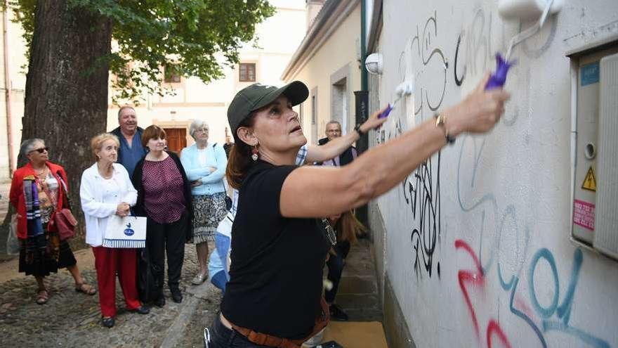 Una vecina pasa una brocha sobre una pintada en una fachada de la plazuela de Santa Bárbara.