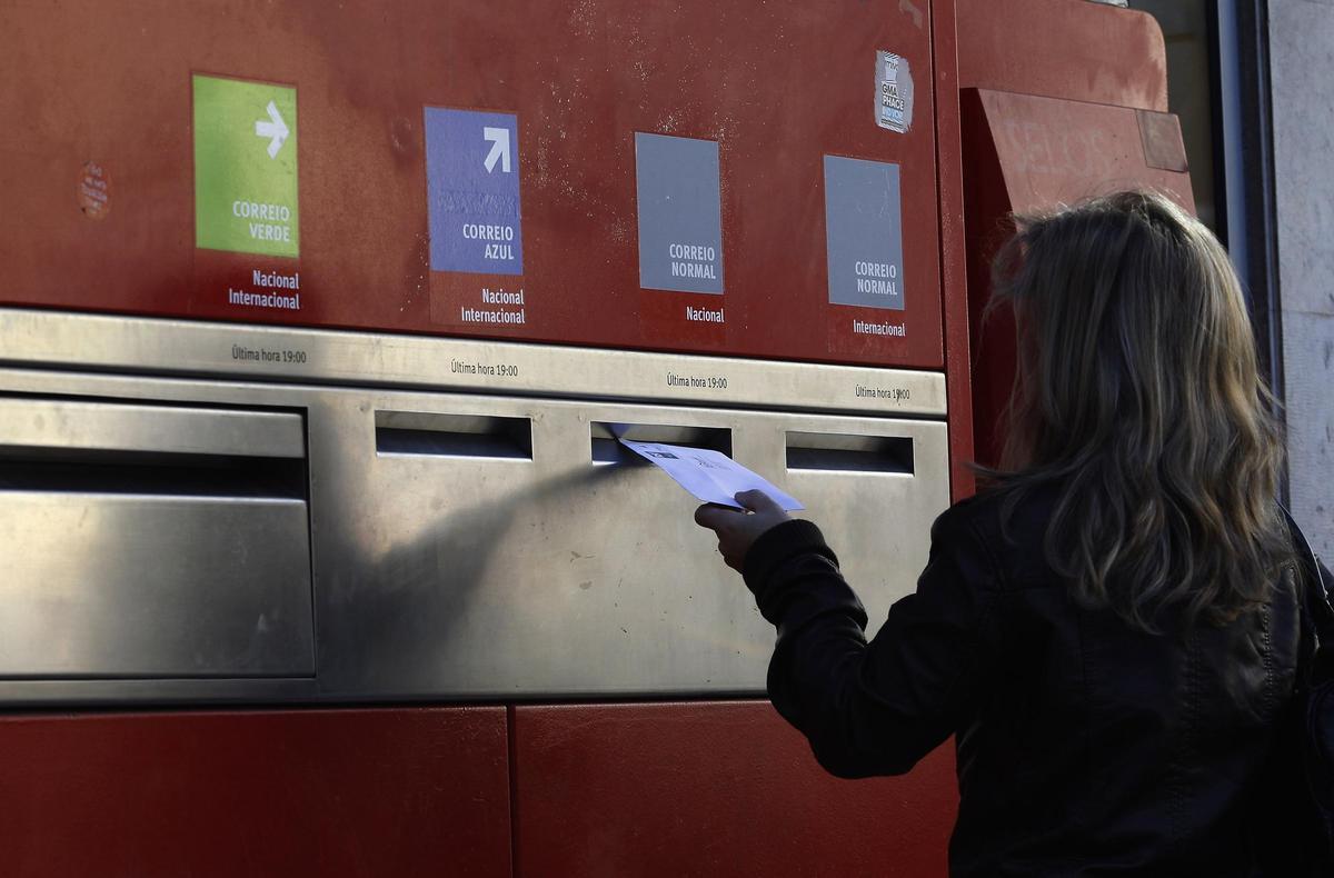 Una mujer deposita una carta en un buzón.
