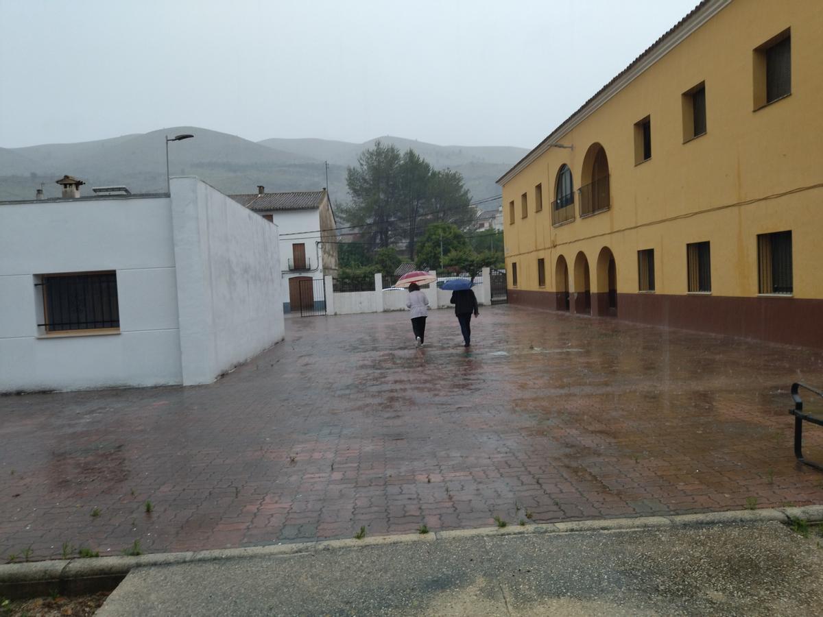 Los primeros votantes, bajo los paraguas, caminan por el patio de la antigua escuela