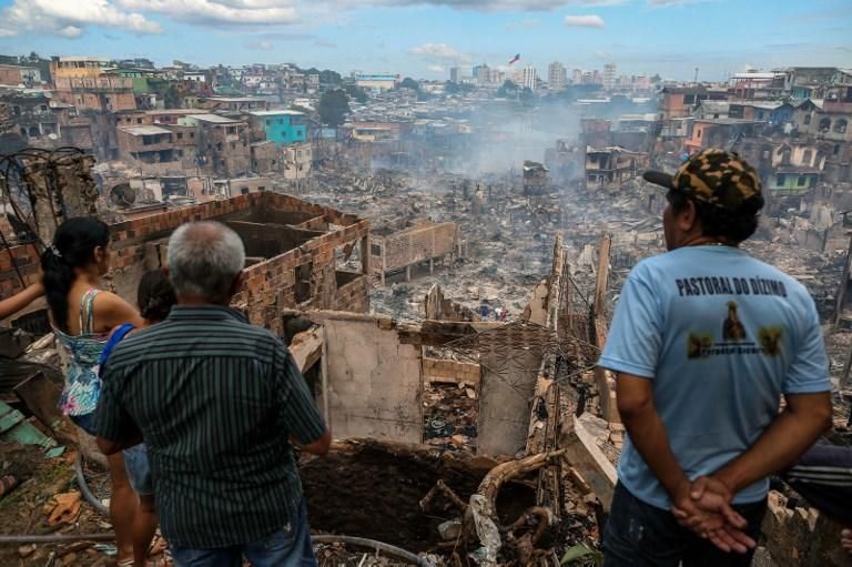 Residentes contemplan los restos del barrio de Edurandos, en Manaus, Brasil, el día después de que fuera asolado por un incendio masivo. - Un incendio inmenso arrasó unas 600 casas de madera construidas cerca de un río en la región amazónica de Brasil, destruyendo una región pobre de la ciudad de Manaus pero sin causar muertes. Una investigación inicial sugiere que un accidente con una olla a presión pudo iniciar el fuego, que se extendió rápidamente, alimentado por fuertes vientos, según las autoridades. 18 de diciembre de 2018. Michael Dantas / AFP