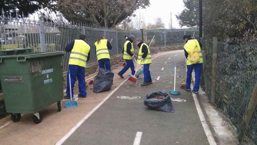 Participantes en el taller de empleo limpian las hojas del carril bici junto a las piscinas.