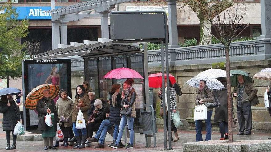 Varios viandantes esperan protegidos con paraguas en una parada de autobús.