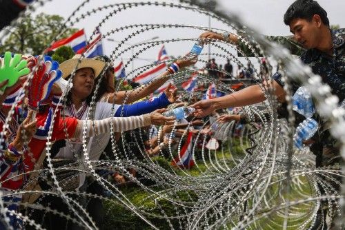 Soldiers hand out bottles of water to anti-government protesters through a barbed-wire fence at a Defence Ministry compound in north Bangkok