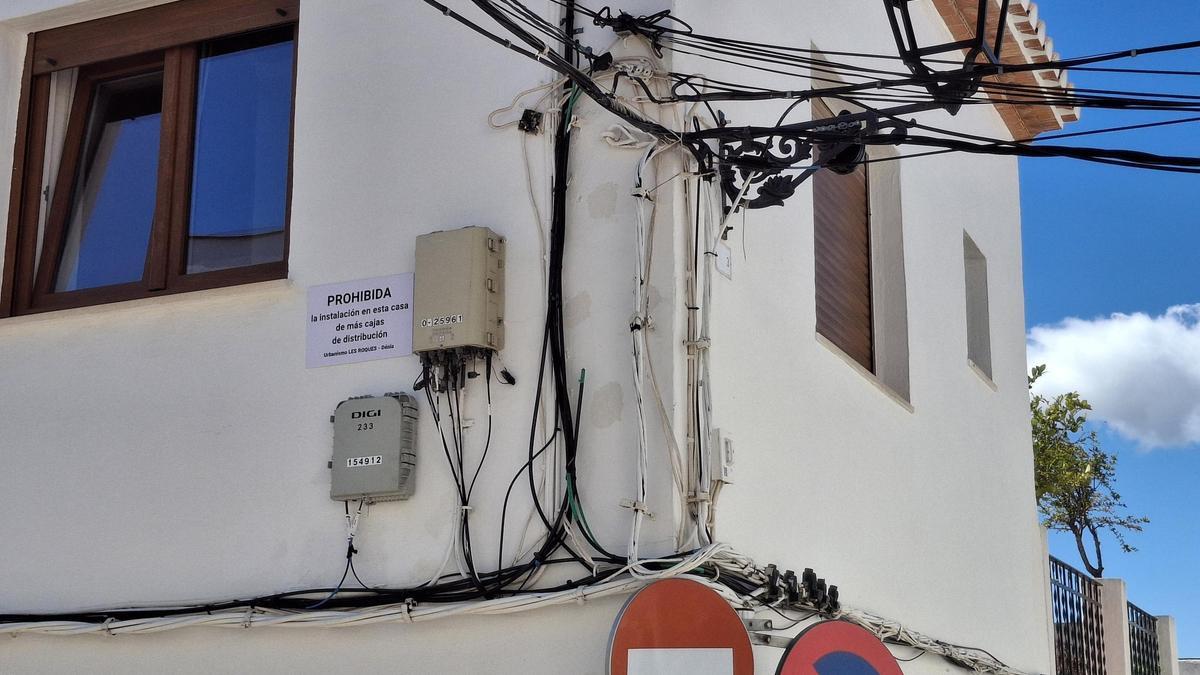 Cartel en una fachada del barrio de les Roques y la maraña de cables