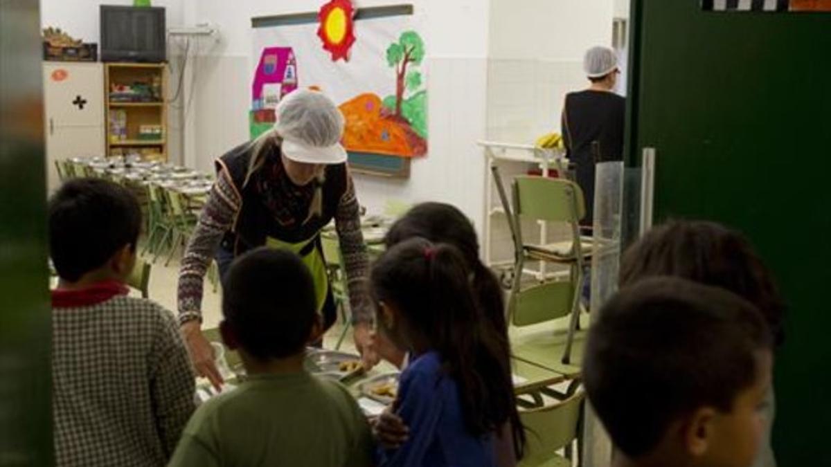 Un grupo de niños aguardan mientas una monitora coloca bandejas con el menú del día en el comedor de la escuela Josep Boada, en Badalona.