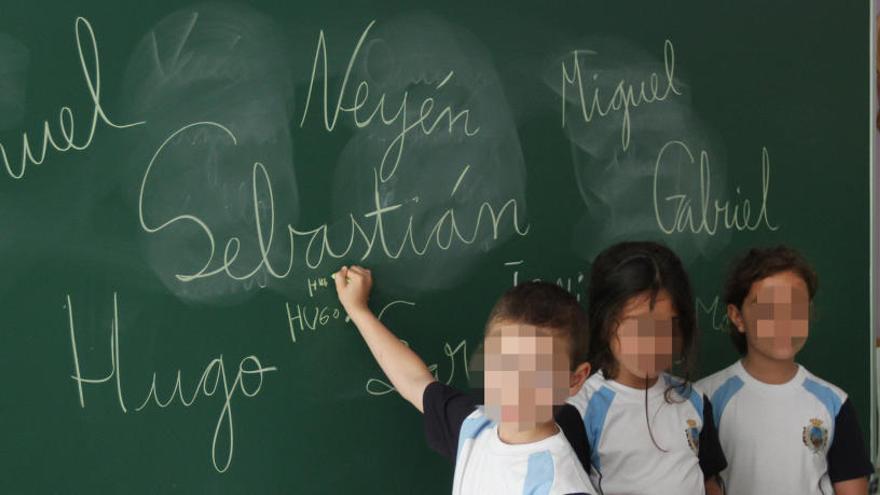 Varios niños escriben sus nombres en la pizarra de su clase.