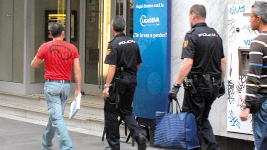 Cuatro agentes de la Policía Nacional, dos de ellos de paisano, ante las puertas de la sucursal bancaria de Triana con una bolsa requisada al detenido.