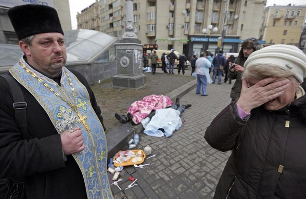 Un sacerdote ortodoxo sostiene una cruz al lado de los cadáveres en la Plaza de la Independencia en Kiev.