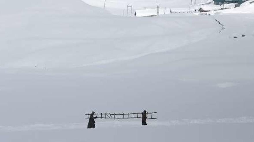 Dos personas llevan una escalera en medio de la nieve.