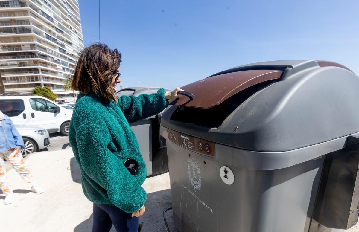 Una mujer abre la tapa de un contenedor marrón, donde se tiran los residuos orgánicos.