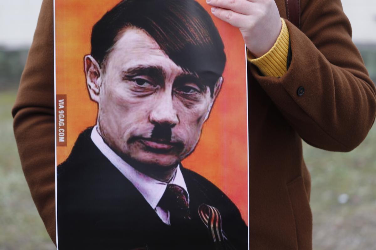 Una persona sostiene una pancarta que muestra a Vladimir Putin vestido como Adolf Hitler mientras la gente protesta contra la operación militar de Rusia en Ucrania, frente a la Embajada de Rusia en Riga, Letonia.