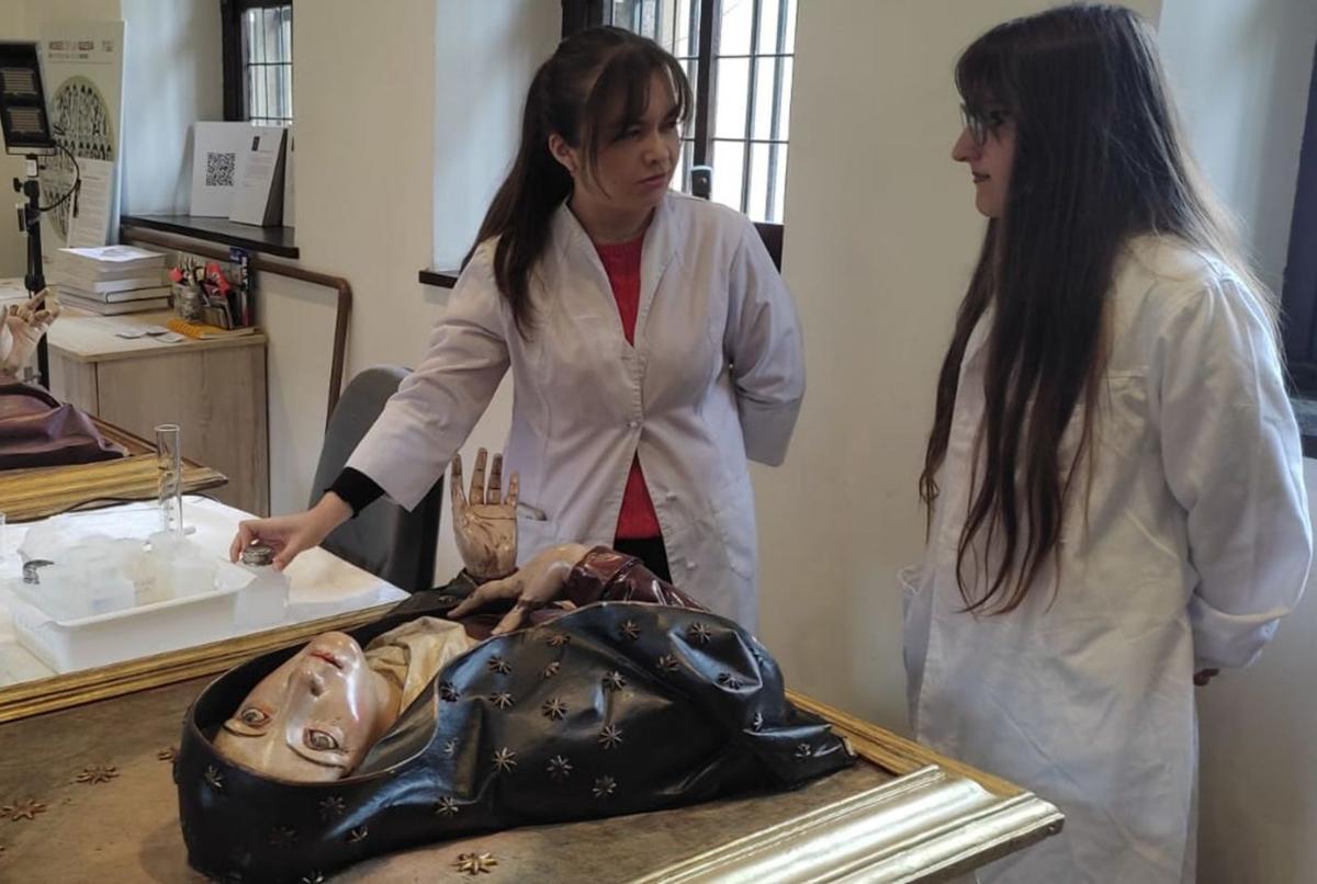 Dos alumnas de la Escuela Superior de Arte, Inés Fernández-Blanco y Laura Tricas Solares, con la imagen de la «Mater Dolorosa» en la que están trabajando en el Museo de la Iglesia de Asturias. | J. A. A.