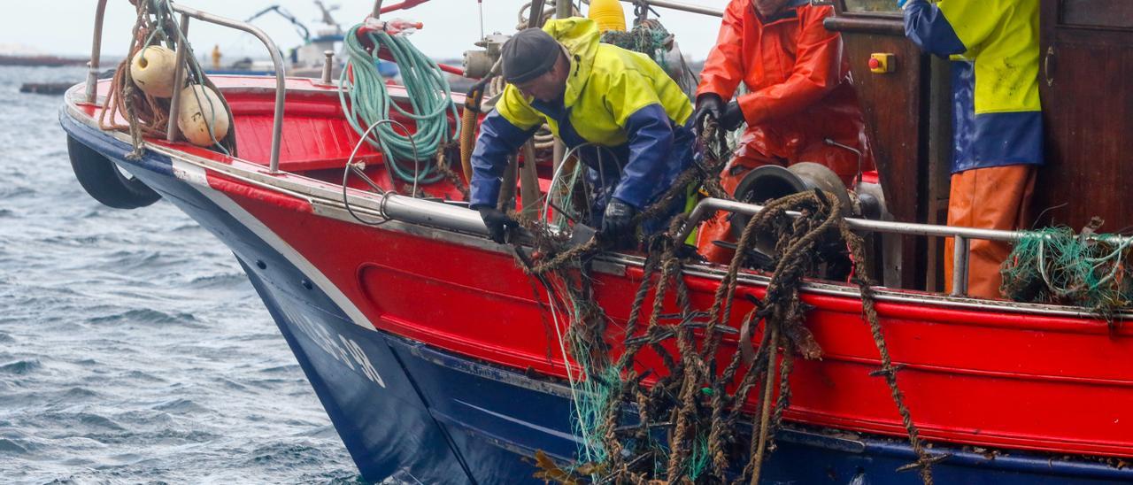 Pescadores de centollo intentando retirar las cuerdas de batea enganchadas en sus “miños”, esta mañana.