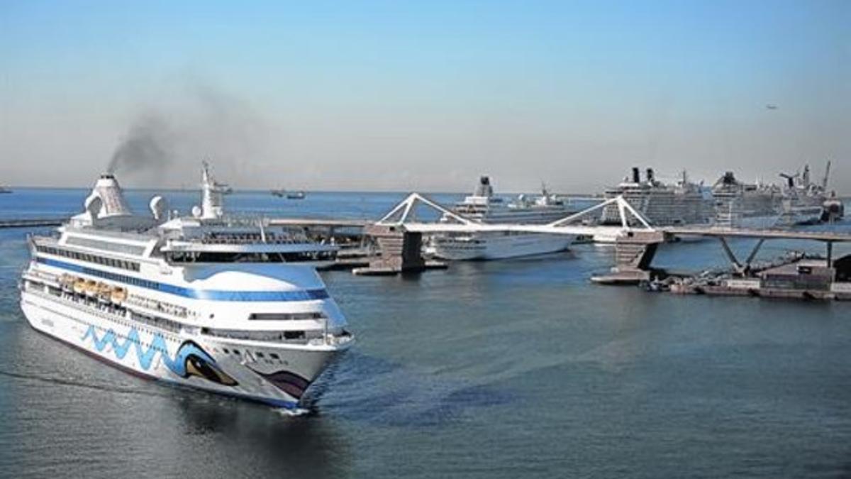 Un ferri humeante entra por la Bocana Nord junto al muelle Adossat repleto de grandes cruceros.