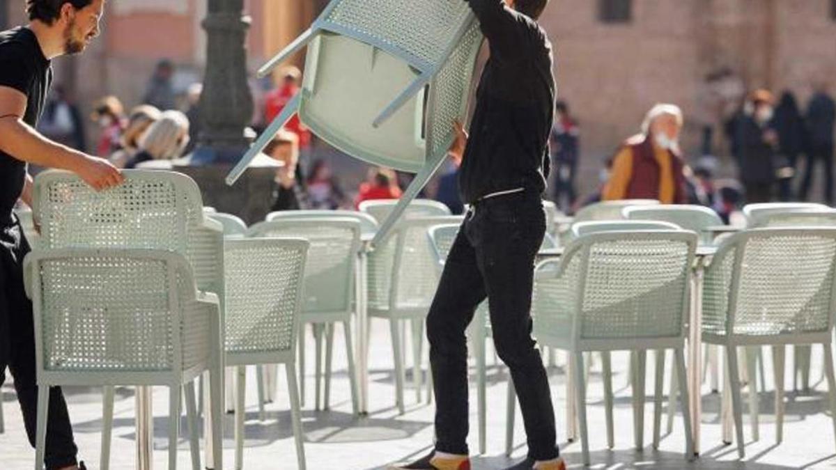 Dos trabajadores de la hostelería colocan sillas en una terraza.