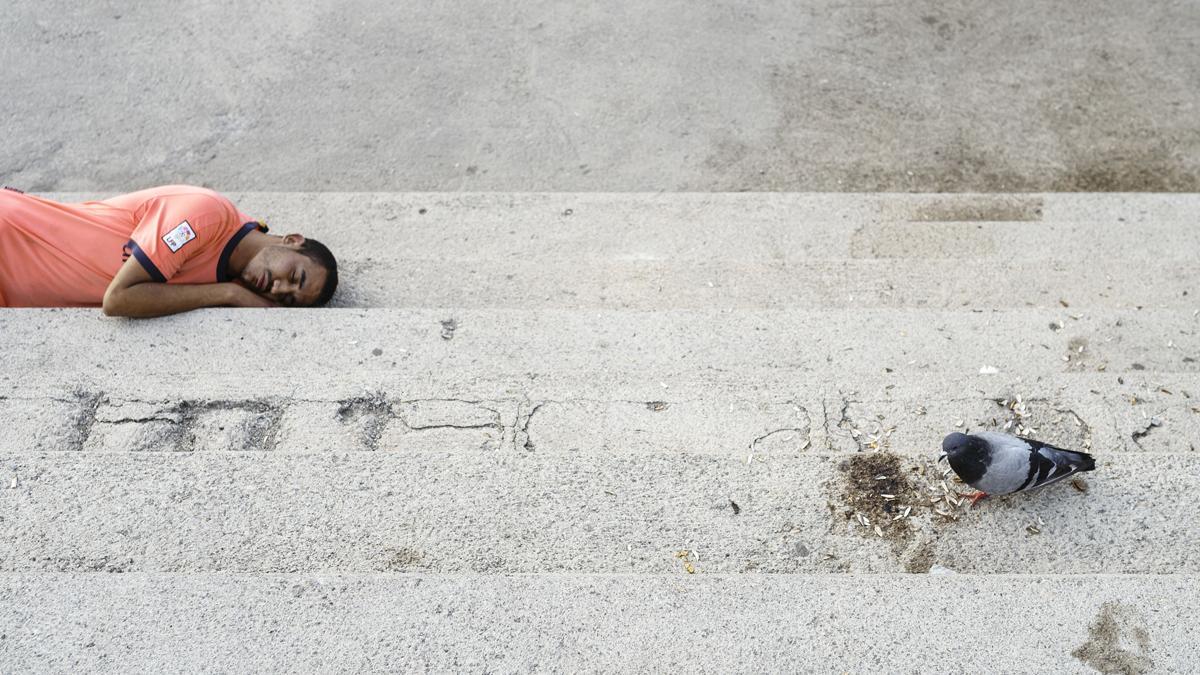 Un hombre descansa en el suelo del Port Olímpic, la mañana del día de Sant Joan.