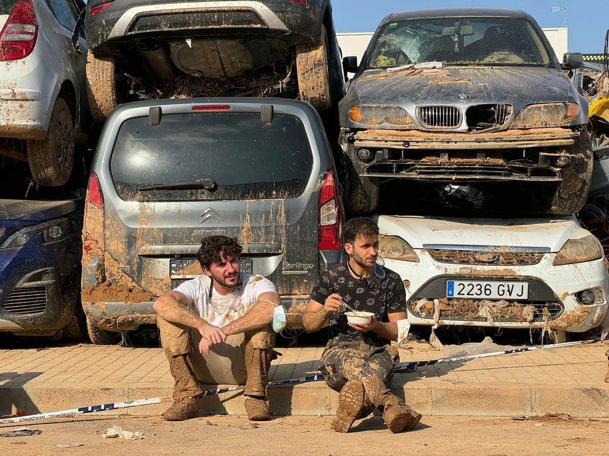 Voluntarios comiendo delante de los coches apilados reocgidos por la grúa.