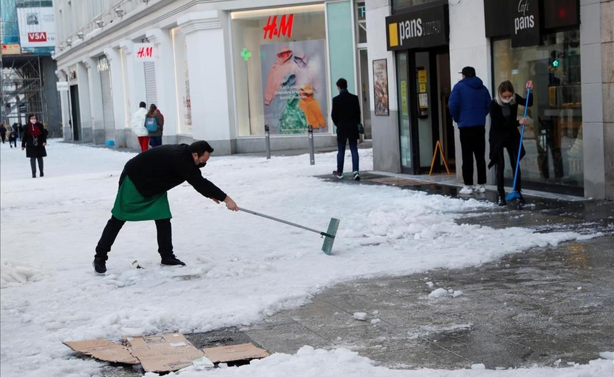 Un empleado de un comercio en la Gran Vía de Madrid retira la nieve de la acera, tras la nevada caída el fin de semana.