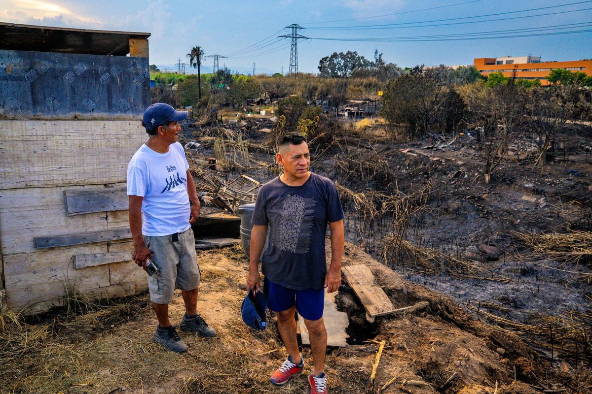 En la zona de barracas cercana al Port de Barcelona, el 1 de julio de 2025, Luis, de 46 años, y Antonio, de 52, observan los estragos del fuego un día después del siniestro. Gran parte del barrio quedó bajo cenizas, lo que aumenta la preocupación de estos vecinos por sus hogares y sus vidas en el asentamiento.