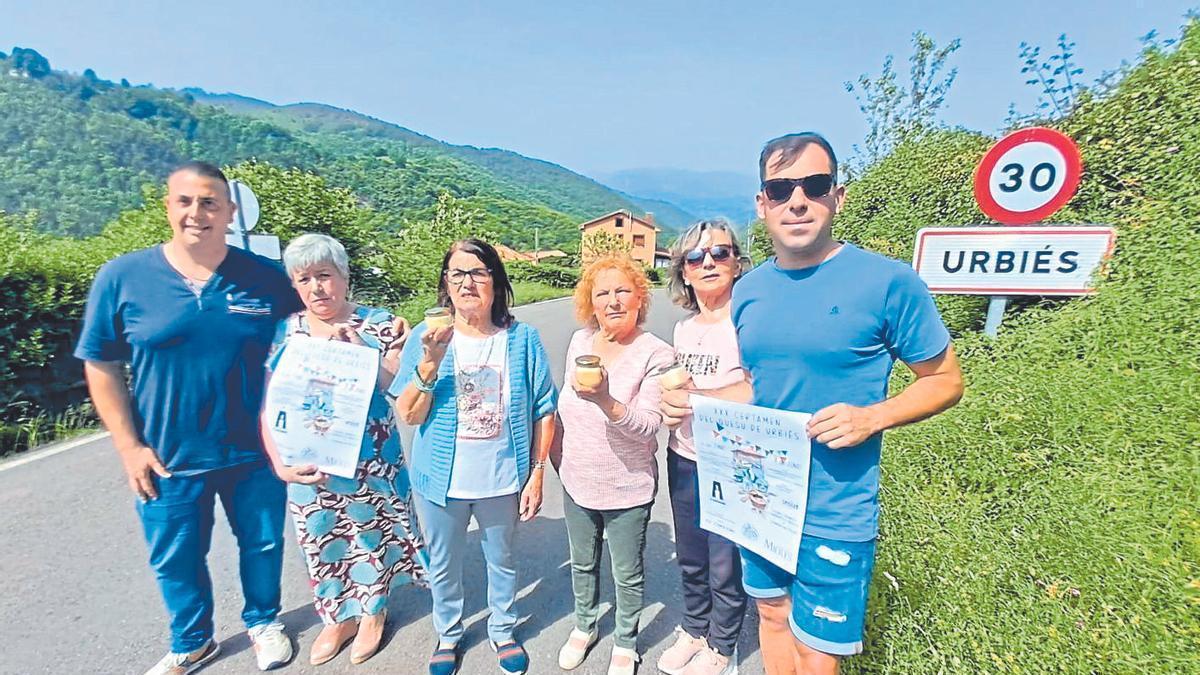 Por la izquierda, Pablo Sánchez, Nardi Iglesias, María Luisa Fidalgo, Geli Crespo, Consuelo Noval y Daniel Fernández, con carteles del certamen del quesu de Urbiés, que cumple 30 años. | D. M.