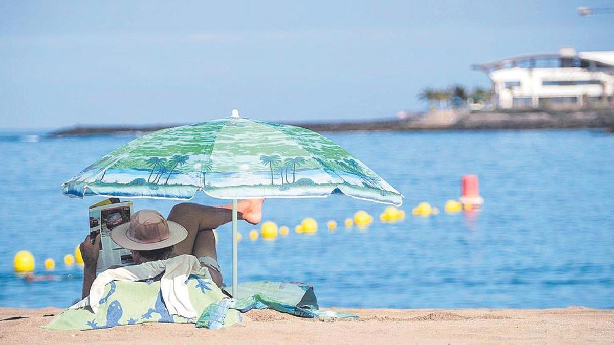Un turista disfruta bajo la sombrilla de la playa de Los Cristianos, al sur de Tenerife.
