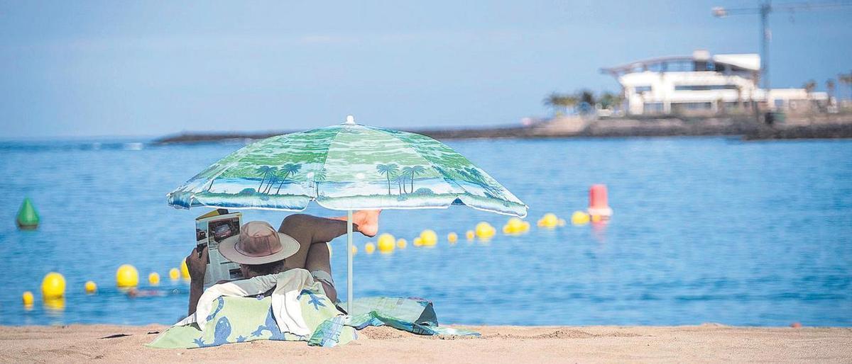 Un turista disfruta bajo la sombrilla de la playa de Los Cristianos, al sur de Tenerife.