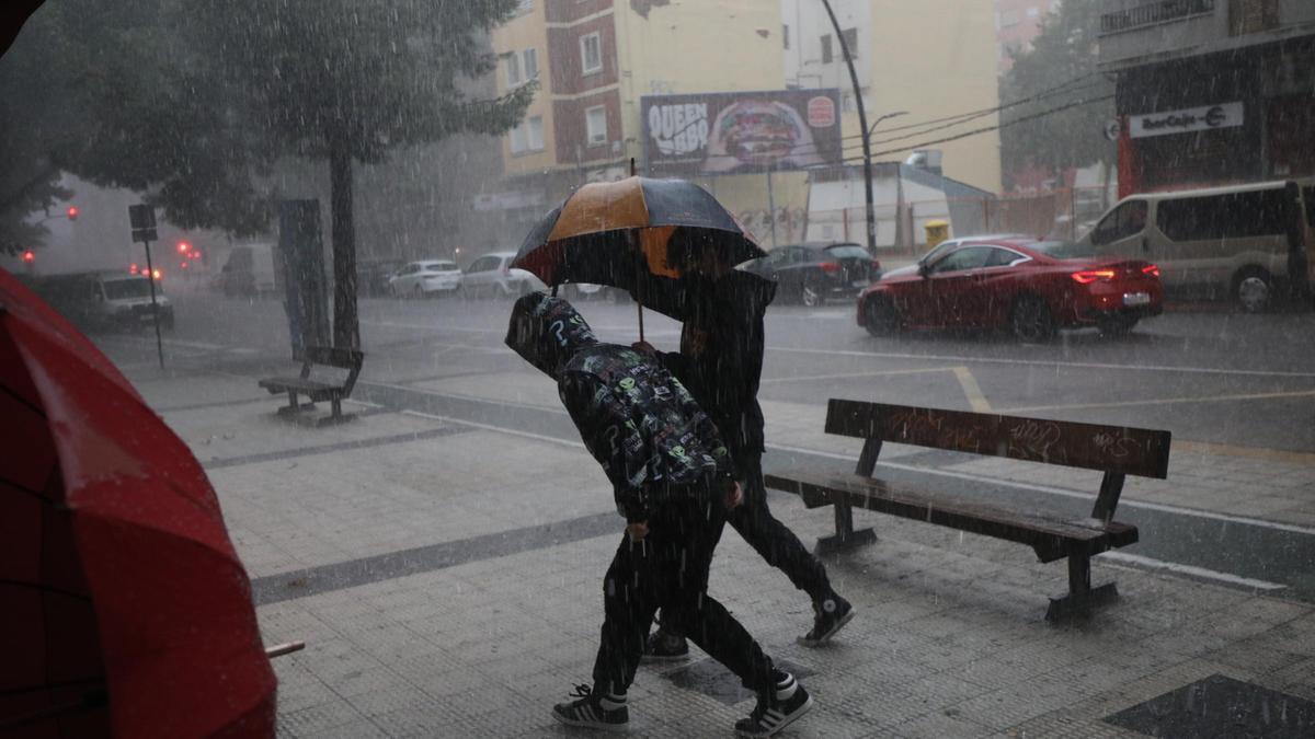 Dos jóvenes se protegen de la tormenta en la calle Sobrarbe de Zaragoza. Imagen de archivo.