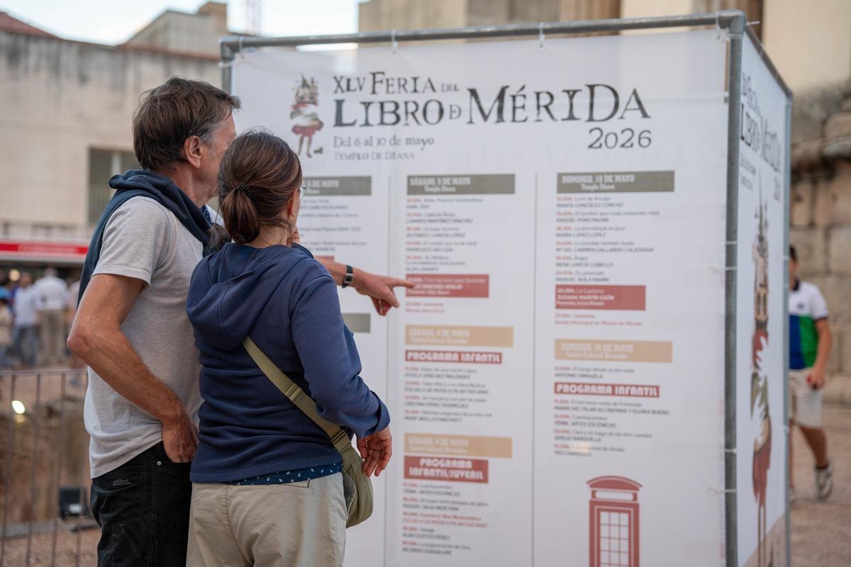 Dos personas consultan la programación de la XLV Feria del Libro de Mérida.